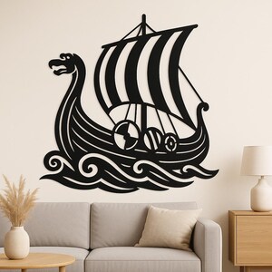 May include: Black metal wall art of a Viking longship. The ship features a detailed design with a dragon head, striped sail, and decorative shields. The artwork is mounted on a neutral-coloured wall, creating a striking contrast. The ship is sailing on stylised waves.