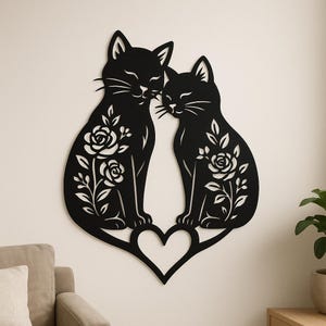 Puede incluir: Arte de pared de metal negro con dos gatos con diseños florales, sentados sobre un corazón. Los gatos se miran, con los ojos cerrados y bigotes. Los diseños florales incluyen rosas y hojas.