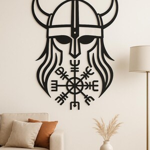 May include: Black metal wall art of a Viking helmet with horns and a central symbol. The artwork has a minimalist design, suitable for home decor. The helmet has a detailed outline, and the symbol is a prominent focal point.
