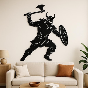 Könnte beinhalten: Schwarze Metall-Wandkunst, die einen Wikingerkrieger in Bewegung zeigt. Die Silhouette zeigt den Krieger mit einer Axt und einem Schild. Geeignet für die Inneneinrichtung, verleiht sie einen Hauch von historischem Flair.