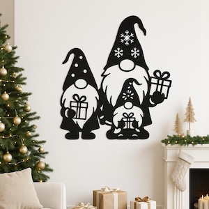 May include: Black metal wall art depicting a family of gnomes holding presents. The gnomes wear tall hats with snowflake and dot details. The artwork is displayed on a white wall, with a Christmas tree and fireplace in the background.