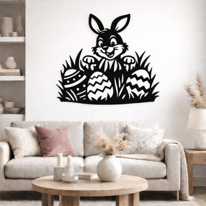 Puede incluir: Arte de pared de metal negro con un conejito de Pascua sonriente mirando por encima de la hierba y tres huevos de Pascua decorados. El conejito tiene orejas largas y está rodeado de hierba y huevos detallados.