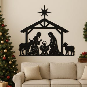 Könnte beinhalten: Schwarze Metall-Wandkunst mit einer Krippenszene. Die Silhouette zeigt die heilige Familie, Tiere und einen Stern. Das Kunstwerk ist über einem beigen Sofa und in der Nähe eines Weihnachtsbaums angebracht.