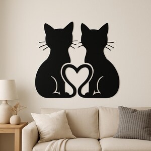 Könnte beinhalten: Schwarze Metall-Wandkunst mit zwei stilisierten Katzen-Silhouetten, die sich gegenüberstehen, mit einem Herz dazwischen. Die Katzen haben Schnurrhaare und sitzen aufrecht. Das Kunstwerk ist an einer neutralfarbenen Wand befestigt.