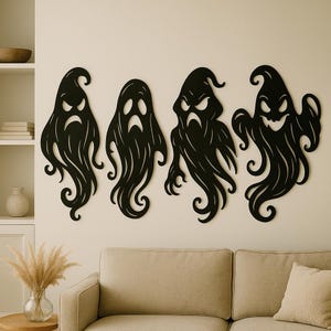 May include: Four black ghost wall decorations with varying expressions. Each ghost has a unique shape and flowing design, perfect for Halloween decor. The ghosts are mounted on a neutral-colored wall, creating a spooky yet stylish ambiance.