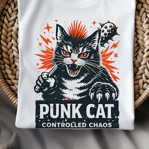 Puede incluir: Camiseta blanca de cuello redondo con un gráfico de gato punk negro y naranja. El gato tiene una cresta y sostiene un garrote con púas. El texto "PUNK CAT" y "CONTROLLED CHAOS" están debajo. El diseño tiene un fondo naranja.