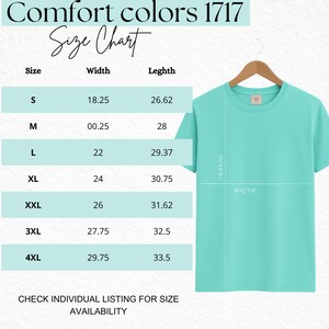 Puede incluir: Una camiseta turquesa claro Comfort Colors 1717 colgada en una percha de madera. La imagen incluye una tabla de tallas con medidas en cm para las tallas S a 4XL. El texto "Size Chart" est&aacute; en la parte superior.