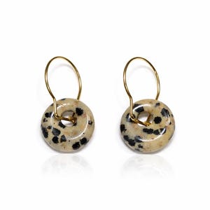 Può includere: Un paio di orecchini con un design circolare in pietra maculata. Gli orecchini hanno macchie nere su sfondo beige e ganci circolari dorati. Su sfondo bianco.