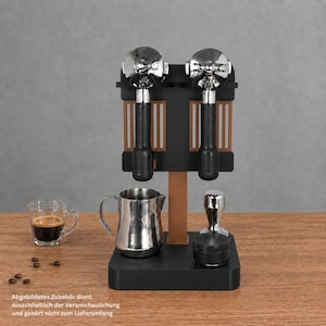Könnte beinhalten: Ein schwarzer und kupferfarbener Espresso-Zubehörständer mit zwei verchromten Siebträgern mit schwarzen Griffen. Darunter stehen ein Milchkännchen aus Edelstahl und ein schwarzer Kaffeetamper auf der Basis. Ein Glas Espresso steht daneben.