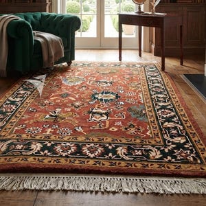 May include: A rectangular area rug featuring a deep red field with intricate floral and equestrian motifs in shades of blue, green, and cream. The rug has a wide black border with floral patterns and a cream-colored fringe along the short edge.