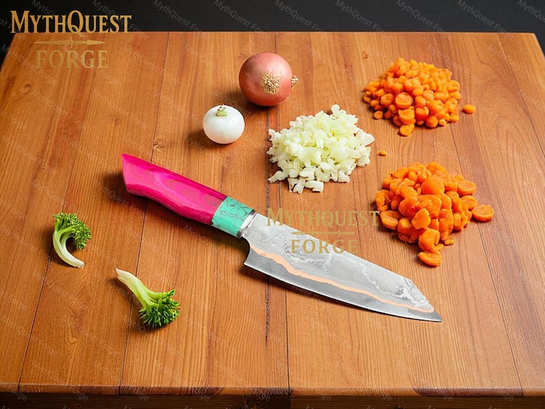 Pode incluir: Uma faca de chef com cabo rosa e verde repousa sobre uma t&aacute;bua de cortar de madeira. Cebolas picadas, cenouras e floretes de br&oacute;colis s&atilde;o dispostos ao redor da faca. A l&acirc;mina da faca tem um padr&atilde;o &uacute;nico. O logotipo MythQuest Forge &eacute; vis&iacute;vel.