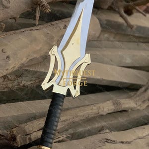 May include: A sword with a silver blade and gold-colored hilt. The hilt has a decorative design and a black, textured grip. The text "MYTHQUEST FORGE" is visible on the hilt.