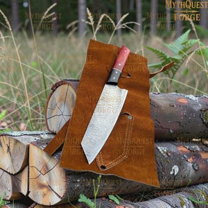 May include: A fixed-blade knife with a patterned metal blade, a black bolster, and a two-tone red and black handle, resting on a brown leather sheath. The blade features a visible layered texture, and the handle is secured with two metal rivets.