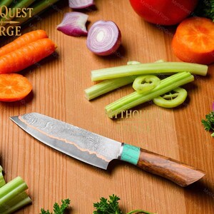 May include: A Damascus steel chef's knife with a wooden handle and turquoise accents rests on a wooden cutting board surrounded by fresh vegetables. The knife has a patterned blade and is designed for kitchen use. The image includes carrots, celery, and onions.