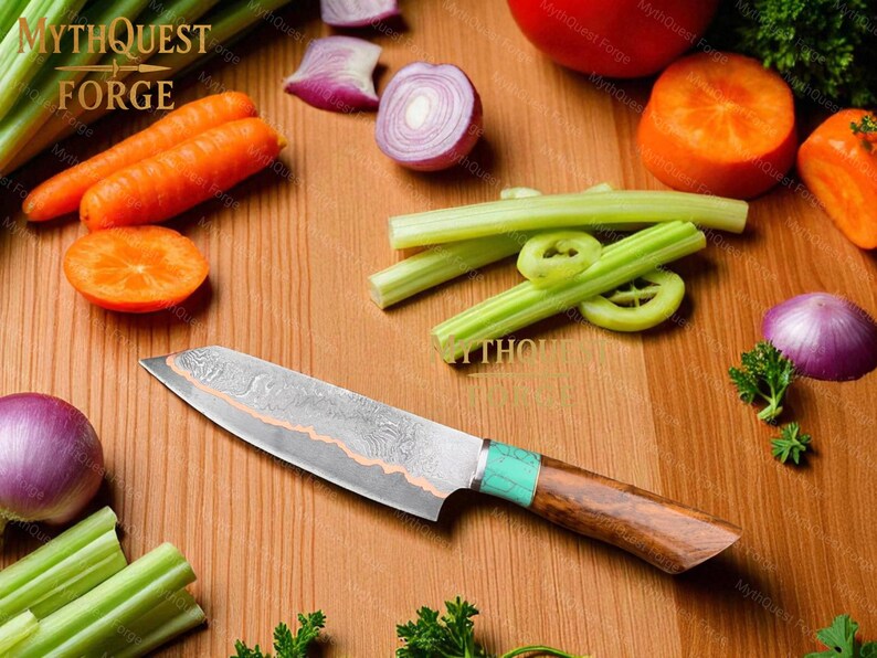 May include: A Damascus steel chef's knife with a wooden handle and turquoise accents rests on a wooden cutting board surrounded by fresh vegetables. The knife has a patterned blade and is designed for kitchen use. The image includes carrots, celery, and onions.