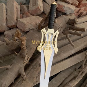 May include: A decorative sword with a gold-colored hilt and a silver blade. The hilt features a black grip and a gold pommel. The sword has the text "MythQuest Forge" on the hilt.