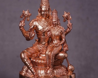 May include: A copper-colored statue depicting two figures, one seated and the other standing, both adorned with ornate headdresses and holding objects. The statue is set against a dark gray background.