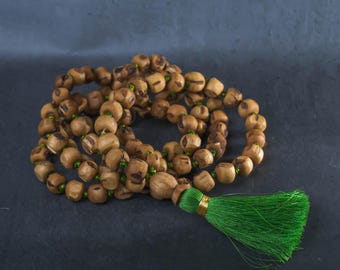 Könnte beinhalten: Eine Kette aus Gebetsperlen mit hellbraunen Holzperlen und grünen Akzenten. Die Perlen sind aufgefädelt, und eine grüne Quaste mit goldenem Besatz hängt am Ende. Die Perlen werden wahrscheinlich für Meditation oder spirituelle Praktiken verwendet.