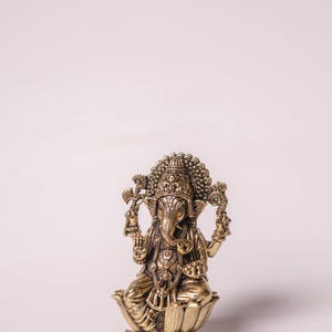 May include: A detailed brass statue of the Hindu deity Ganesha, seated on a lotus flower. The statue features intricate carvings, a large head, and multiple arms holding various objects. The figure is adorned with ornate jewelry and a crown.