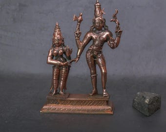May include: Bronze statues of a male and female deity. The male figure holds a weapon and a curved object. The female figure stands beside him. Both figures have ornate headdresses and are on a decorative base. A dark stone sits to the side.