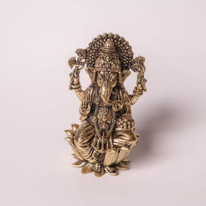 May include: A detailed brass statue of the Hindu deity Ganesha, seated on a lotus flower. The statue features intricate carvings, a large head with elephant features, and multiple arms holding various objects. The figure is adorned with ornate jewelry and a crown.