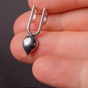 May include: A silver-colored earring with a teardrop-shaped charm. The earring has a U-shaped top that curves around the earlobe. The charm is smooth and polished, reflecting light.