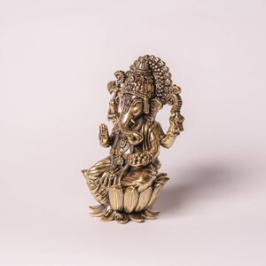May include: A detailed brass statue of the Hindu deity Ganesha, seated on a lotus flower. The statue features intricate carvings, a large head with elephant features, and multiple arms. The figure is in a seated position with hands in a blessing gesture.