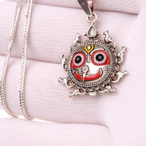 Puede incluir: Collar con colgante de plata con un diseño de rostro detallado y colorido. El colgante tiene detalles en rojo, amarillo y negro, y está unido a una delicada cadena de plata. El colgante mide aproximadamente 3,8 cm de diámetro.