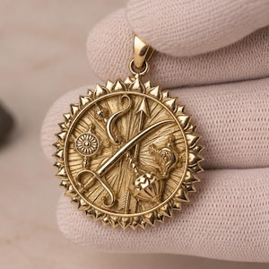 May include: A circular gold pendant featuring a detailed relief design of a sword, bow, arrow, mace, and conch shell. The outer edge of the pendant is decorated with a sunburst pattern of pointed rays, and it includes a small bail at the top.