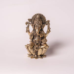 May include: A detailed brass statue of the Hindu deity Ganesha, seated on a lotus flower. The statue features intricate carvings, a large head with elephant features, and multiple arms holding various objects. The figure is in a seated position.