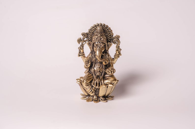 May include: A detailed brass statue of the Hindu deity Ganesha, seated on a lotus flower. The statue features intricate carvings, a large head with elephant features, and multiple arms holding various objects. The figure is in a seated position.