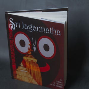 Puede incluir: Un libro de tapa dura titulado "Sri Jagannatha" con una cubierta roja y negra. La cubierta presenta un gráfico de grandes ojos blancos y una ilustración de un templo. El título del libro está en blanco y el subtítulo dice "Los pasatiempos del Señor del Universo."