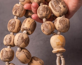 Könnte beinhalten: Eine Kette aus Holzperlen mit einem natürlichen Holzmaserungsmuster. Die Perlen sind rund und durch ein helles Seil verbunden. Die Perlen werden in einer Hand vor grauem Hintergrund gehalten.