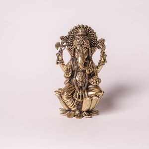 May include: A detailed golden statue of the Hindu deity Ganesha, seated on a lotus flower. The statue features intricate carvings, a large head with elephant features, and multiple arms holding various objects. The figure is adorned with ornate jewelry and a crown.