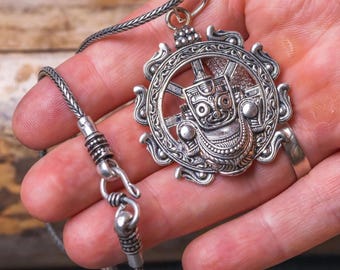 Puede incluir: Collar con colgante de plata con un colgante circular detallado. El colgante presenta una figura central dentro de un diseño intrincado. Cuelga de una cadena tejida con un cierre seguro. El diseño es intrincado y tiene un aspecto vintage.