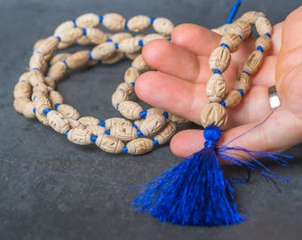 Könnte beinhalten: Eine beige Gebetskette mit blauen Akzenten und einer blauen Quaste. Die Perlen sind mit einem sich wiederholenden Muster geschnitzt und auf einer blauen Schnur aufgefädelt. Die Quaste besteht aus blauen Fäden.