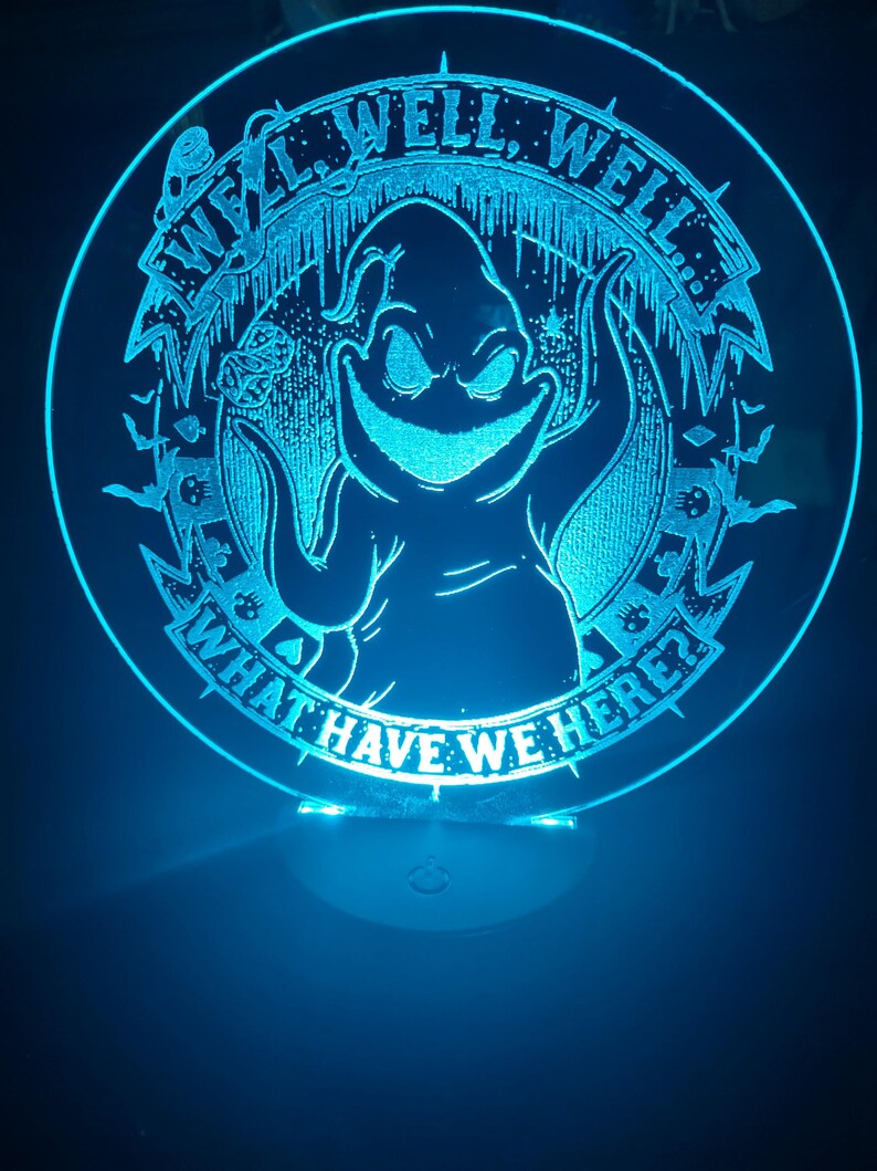 May include: A round, illuminated acrylic sign with a blue glow. The sign features a cartoon character with the text "Well, Well, Well... What Have We Here?" in a circular design. The design includes bats and other spooky elements.