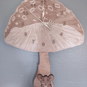 May include: Wooden mushroom-shaped wall clock with a light brown cap featuring white spots and a detailed stem. The clock face has silver hands and numbers. A small, smiling mouse is at the base of the stem.