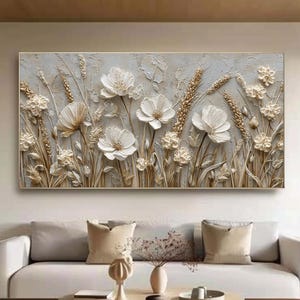 Puede incluir: Obra de arte mural enmarcada con un diseño floral en 3D. La obra presenta flores blancas y espigas de trigo sobre un fondo gris claro texturizado. El marco es de color neutro, complementando los tonos suaves de las flores.