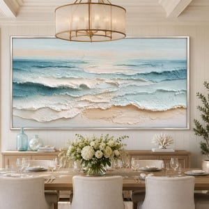 May include: A large rectangular wall art piece featuring a textured oil painting of an ocean scene with rolling waves in shades of blue, white, and beige sand. The artwork is framed in a thin silver border and depicts a calm coastal landscape.