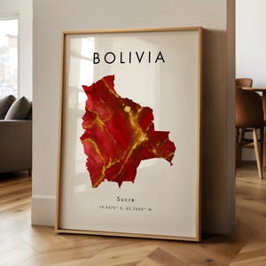 Könnte beinhalten: Gerahmter Kunstdruck mit einer Karte von Bolivien in Rot- und Goldtönen. Das Wort "BOLIVIA" ist oben aufgedruckt, darunter "Sucre" und Koordinaten. Das Kunstwerk wird in einem Raum mit Holzboden ausgestellt.