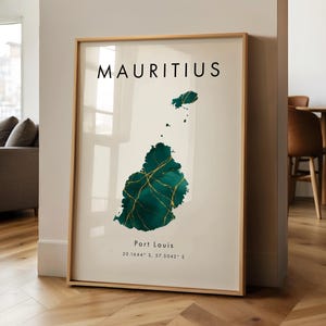 Op de afbeelding: Een ingelijste kunstdruk met een kaart van Mauritius in groen- en goudtinten. Het woord "MAURITIUS" staat in zwarte letters bovenaan, met "Port Louis" en coördinaten eronder. De print zit in een houten lijst.