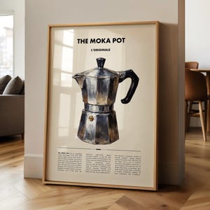 May include: A framed print displaying a watercolour illustration of a Moka Pot, with the text "THE MOKA POT" and "L'ORIGINALE". The print has a light beige background and is displayed in a room with hardwood flooring.