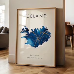 Könnte beinhalten: Gerahmter Kunstdruck mit einer Karte von Island in Blau mit goldenen Adern. Das Wort "ICELAND" steht oben, darunter "Reykjavik" und Koordinaten. Das Kunstwerk ist in einem hellen Holzrahmen.