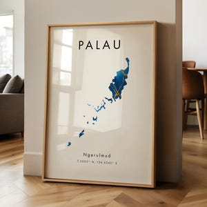 May include: A framed print of the Palau map, with blue and gold detailing on a cream backdrop. The word "PALAU" is at the top, with "Ngerulmud" and coordinates below. The frame is a light wood colour.