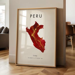 May include: Framed art print featuring a map of Peru in shades of red and gold. The word "PERU" is printed at the top, with "Lima" and coordinates below. The artwork is displayed in a room with hardwood floors.