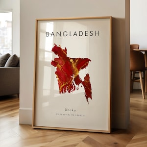 May include: Framed art print showing a map of Bangladesh in red and gold. The word "BANGLADESH" is printed at the top, with "Dhaka" and coordinates below. The artwork is displayed in a room with a wooden floor.