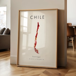 May include: A framed art print displaying a map of Chile in red and yellow tones on a cream backdrop. The word "CHILE" is printed at the top, with "Santiago" and coordinates below. The print is enclosed in a light wood frame.