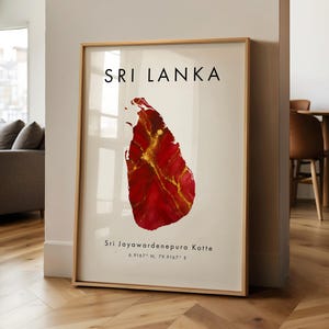 Peut inclure: Impression encadrée représentant le Sri Lanka. La carte du pays est en rouge et or. Le texte "SRI LANKA" est en haut, avec "Sri Jayawardenepura Kotte" et des coordonnées en dessous. Cadre en bois clair.