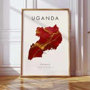 Könnte beinhalten: Gerahmter Kunstdruck mit dem Wort "UGANDA" in schwarzen Großbuchstaben über einer rot-goldenen Karte von Uganda. Die Stadt Kampala und ihre Koordinaten sind darunter abgedruckt. Der Rahmen ist hellbraun.